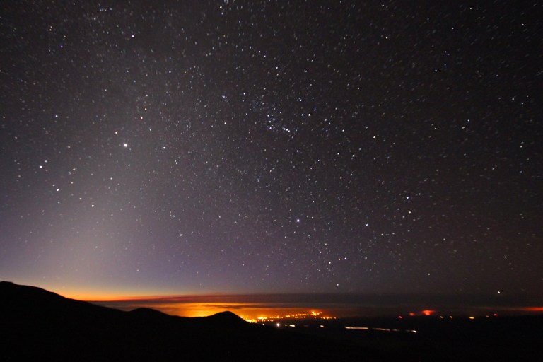 Pre-twilight overlooking Hilo. Zodiacal light is seen extending diagonally from the lower left of the frame. The Milky Way intersects the zodiacal light, extending diagonally from the right.