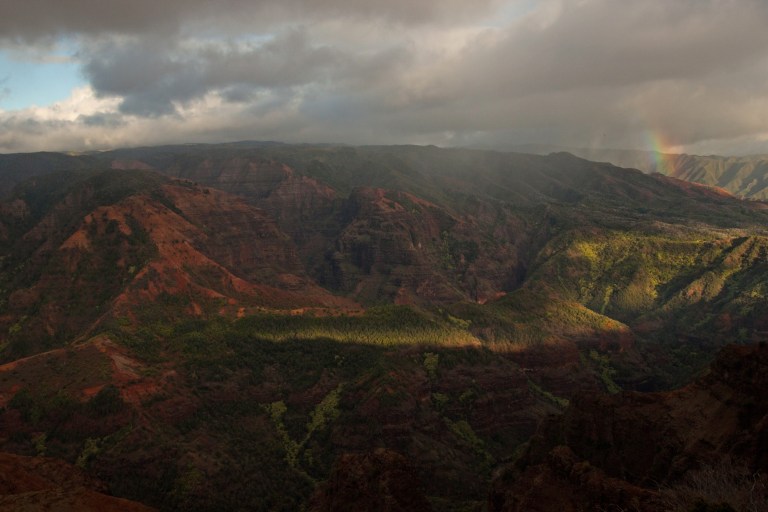 One last look at Waimea Canyon on the way out of the park, with the sun low on the horizon and a surprise rainbow diving into the canyon.