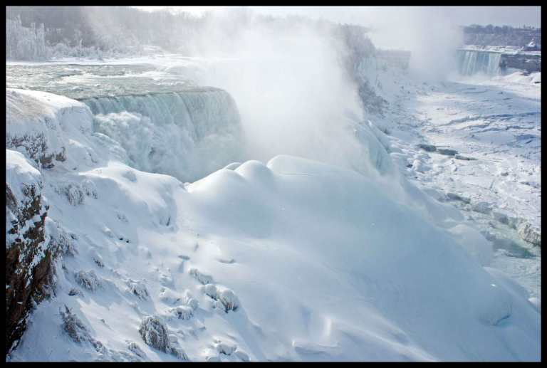 A winter's worth of snow drifts built up against the partially frozen falls, and an almost completely frozen river.